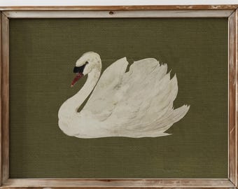 May include: A framed artwork featuring a white swan with a black beak and red mouth, set against a textured olive green background. The swan is painted with detailed feathers. The frame is made of wood.