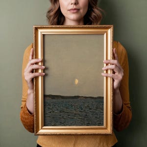 May include: A framed landscape painting with a gold ornate frame. The artwork depicts a seascape with a pale yellow moon in a muted sky. The water is dark blue, and a dark land mass is visible in the distance.