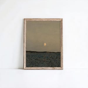 May include: A framed landscape print featuring a serene seascape under a dusky sky. The artwork depicts a body of water, a distant shoreline, and a crescent moon. The frame is a light, natural wood tone, adding a rustic touch to the artwork.