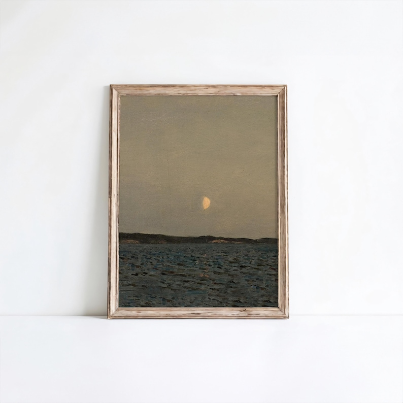 May include: A framed landscape print featuring a serene seascape under a dusky sky. The artwork depicts a body of water, a distant shoreline, and a crescent moon. The frame is a light, natural wood tone, adding a rustic touch to the artwork.