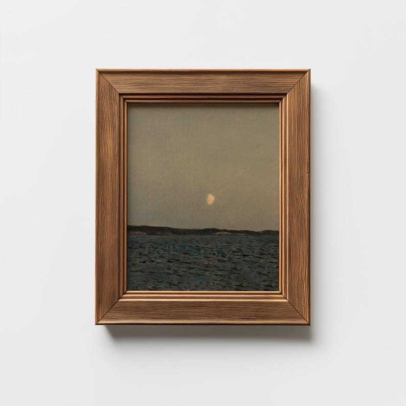 May include: A framed landscape painting depicting a seascape under a dusky sky. The artwork features a moon and dark blue water, framed in a brown wooden frame. The painting evokes a sense of tranquility and natural beauty.