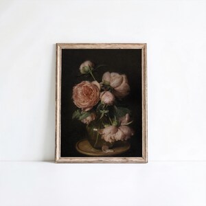 May include: A framed floral print featuring a bouquet of pink peonies in a clear glass vase. The flowers are in various stages of bloom, with lush petals and green foliage. The background is dark, and the frame is a light wood color.