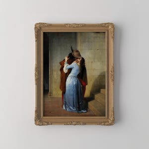 Pu&ograve; includere: Stampa incorniciata di un dipinto classico raffigurante un abbraccio romantico. L'opera presenta un uomo con cappotto e cappello marrone che bacia una donna con un vestito blu. La cornice &egrave; ornata con una finitura dorata.