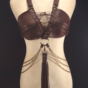 May include: A brown leather halter top with a lace-up front and a chain and tassel detail.