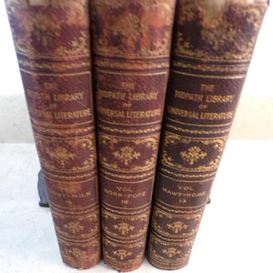 May include: Three antique books with brown and gold covers. The spines display the title "The Ridpath Library of Universal Literature" and volume numbers. The covers have ornate gold patterns and the text "Vol" and the author's last name.