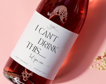 May include: A bottle of rosé wine with a white label that reads "I CAN'T DRINK THIS... but you can." The label also includes the name "Baby Swanson" and the date "February 2020." The wine is on a pink surface.