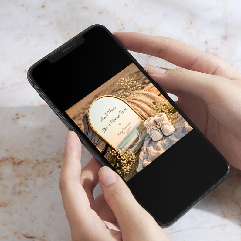 May include: A black smartphone displaying an arched sign with the text And Then There Were Five, Baby Surname, and 2024. The sign is decorated with small white flowers and sits next to a pair of tiny cream-colored knitted baby booties on a textured fabric.
