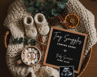 May include: A cozy basket holds a cream-colored knitted blanket, baby booties, and a mug with marshmallows spelling "BABY." A letterboard announces "Tiny Snuggles, Coming Soon!" with a sonogram image, pine sprigs, and cinnamon sticks.