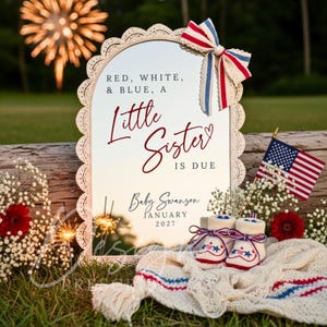 May include: A patriotic pregnancy announcement with a mirror frame, text reading "RED, WHITE, & BLUE, A Little Sister IS DUE, Baby Swanson, JANUARY 2027." Features baby booties, an American flag, and a red, white, and blue bow.