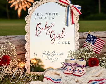 Puede incluir: Un anuncio de bebé patriótico con un espejo que dice "Red, White, & Blue, A Baby Girl Is Due" y "Baby Swanson January 2027." La escena incluye patucos, una manta y una bandera estadounidense.