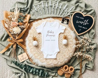 May include: A white baby onesie with the text "Baby Morris JUNE 2020" is centered on a woven mat. The image includes a bouquet, ultrasound photo, heart-shaped sign reading "YOU ARE WORTH THE WAIT", and baby booties. Syringes are arranged at the top.