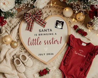 May include: A heart-shaped announcement board with the text "SANTA IS BRINGING A little sister!" and "JULY 2026". A red onesie with ruffles and the name "Swanson" is next to a pair of baby shoes and a floral headband. A plaid bow is at the top.