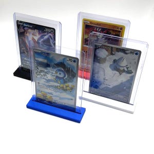 May include: Four clear acrylic card holders displaying collectible cards. The cards feature various characters and text, including "Darkrai," "Piplup," "Groudon," and "Snover." The holders have black, blue, and white bases.