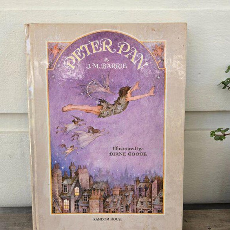 May include: A vintage hardcover book titled "Peter Pan" by J.M. Barrie, illustrated by Diane Goode. The cover features a purple background with an illustration of Peter Pan flying above a cityscape. The Random House logo is at the bottom.