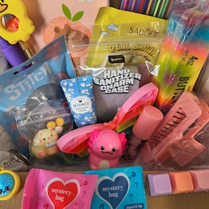 May include: A gift box containing a variety of items including a yellow duck rattle, a Stitch-themed pouch, a Bluebell hand cream, a hand sanitizer charm case, a pink axolotl figure, a rainbow slime container, a hair clip, and mystery bags.