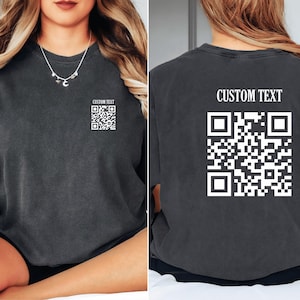 May include: A black t-shirt with a white QR code and the text "CUSTOM TEXT" printed on the back. The front of the shirt has a smaller QR code with the text "CUSTOM TEXT" printed above it.