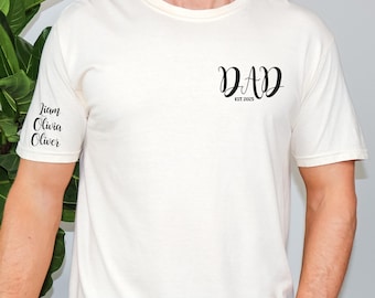 May include: Cream-colored t-shirt with the word "DAD" in a script font and the text "EST 2025". The names Liam, Olivia, and Oliver are printed on the left sleeve in black script. A simple, personalized design.