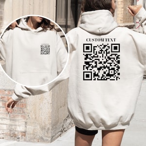 Könnte beinhalten: Weißer Hoodie mit einem schwarzen QR-Code und dem Text "CUSTOM TEXT" auf der Rückseite.