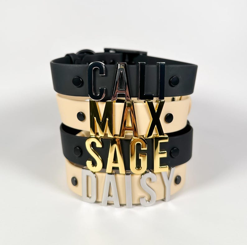 Puede incluir: Collares para mascotas apilados en negro y crema, cada uno con un nombre escrito en letras met&aacute;licas: Cali, Max, Sage y Daisy. Los collares tienen un dise&ntilde;o sencillo y moderno con cierre de hebilla.