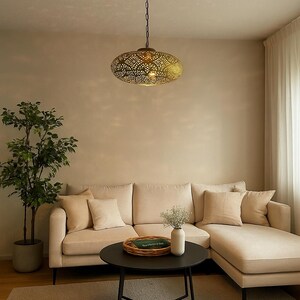 May include: A decorative, oval-shaped pendant light fixture with an intricate, openwork design. The light is suspended from a chain and casts a warm glow. The fixture is made of a metallic material and is a focal point in a living room setting.