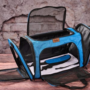 May include: Open blue pet carrier with black mesh windows and a handle. The carrier has a blue interior with a white pad and a blue strap. The carrier has the word "lulu" on a brown tag.