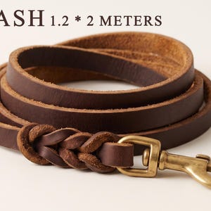May include: A dark brown leather leash coiled in a circle, featuring a braided section near a brass swivel snap hook. The text LEASH 1.2 * 2 METERS is printed above the leash, indicating the dimensions of the leather strap in meters.