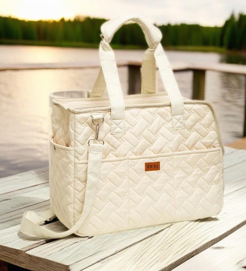 May include: A white quilted tote bag with a long shoulder strap and a zippered closure. The bag has a small pocket on the front with the word "DEMI" printed on it.