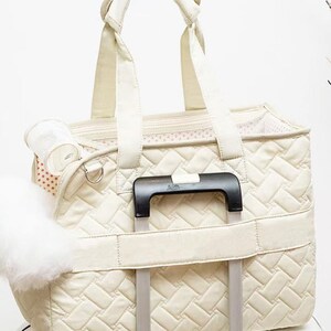 May include: A cream-colored quilted pet carrier with a mesh window and a handle. The carrier has a strap to attach to a rolling suitcase.