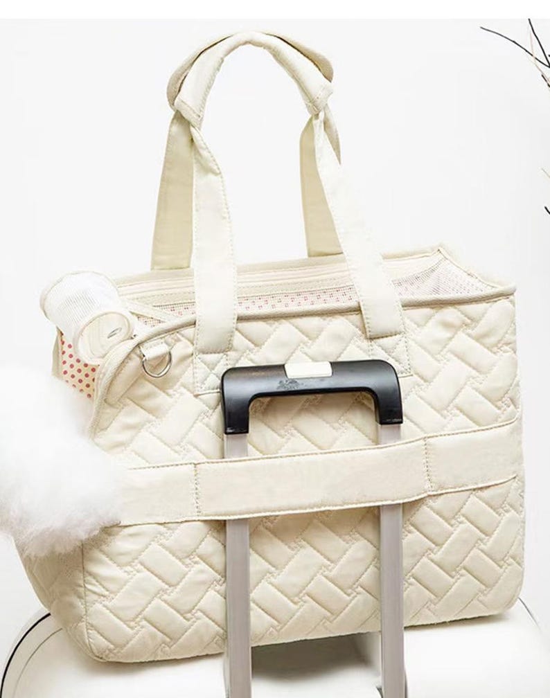 May include: A cream-colored quilted pet carrier with a mesh window and a handle. The carrier has a strap to attach to a rolling suitcase.