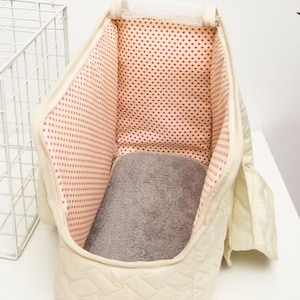 May include: A white quilted pet carrier with a red polka dot lining and a gray fleece bed. The carrier has a mesh top and a zippered opening.
