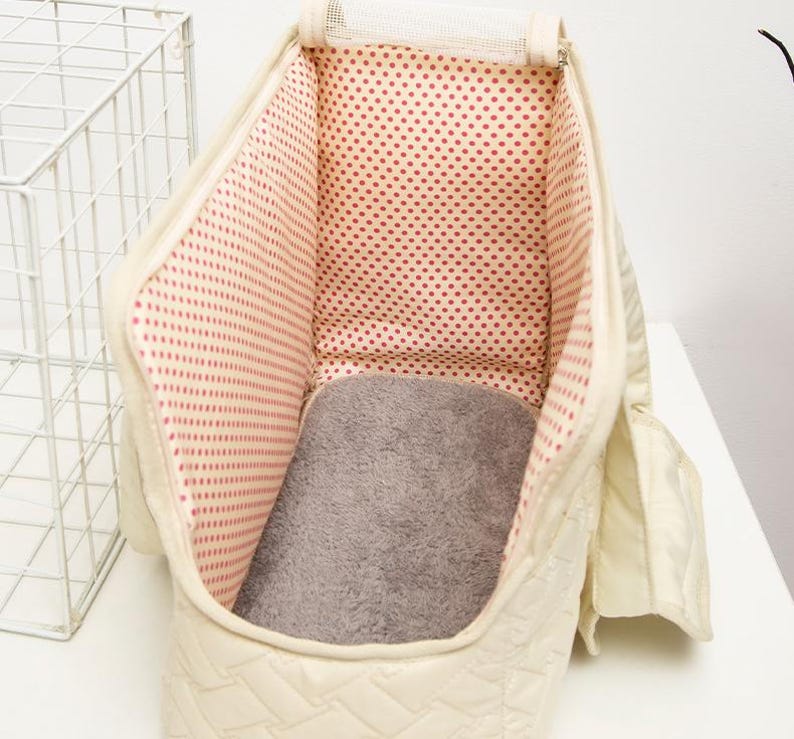 May include: A white quilted pet carrier with a red polka dot lining and a gray fleece bed. The carrier has a mesh top and a zippered opening.