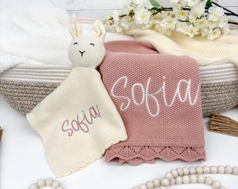 May include: A pink baby blanket and a cream-colored security blanket with the name "Sofia" embroidered in white and mauve thread. A cream-colored bunny head is attached to the security blanket. The blanket has a scalloped edge.