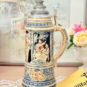 Peut inclure: Une chope à bière en céramique avec une base de couleur crème et des détails en relief bleus. La chope comporte un couvercle en métal avec un levier et une anse. Le corps présente des scènes complexes de personnages et des motifs décoratifs.