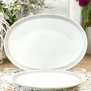 Op de afbeelding: Twee witte ovale serveerschalen met een dunne grijze streep rond de rand. De schalen zijn op elkaar gestapeld.