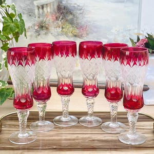 Könnte beinhalten: Satz von sechs roten und klaren Champagnerflöten aus Glas mit geschliffenem Glasdesign. Die Flöten haben eine hohe, schlanke Form mit einem zarten Stiel.