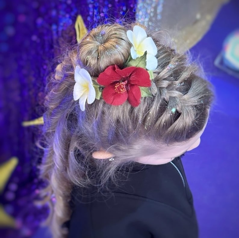 May include: A hairstyle featuring blonde hair styled with a braid and bun, adorned with white and red fabric flowers. The hair is sprinkled with glitter, creating a festive and decorative look.
