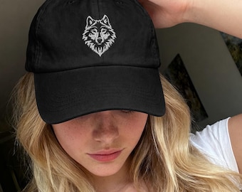 May include: A black baseball cap featuring a white embroidered wolf head design centered on the front panel. The cap has a curved brim and a structured crown, constructed from a solid black fabric with matching stitching throughout the design.