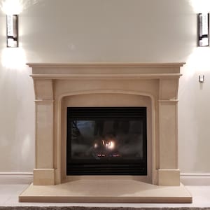 May include: A beige stone fireplace with a black firebox. The fireplace has a rectangular design with a curved arch above the firebox. Two sconces are mounted on the wall on either side of the fireplace.