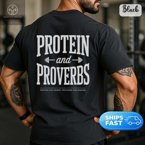 Könnte beinhalten: Ein schwarzes kurzärmeliges T-Shirt mit weißem Text auf der Rückseite, der PROTEIN and PROVERBS lautet, mit einem Hantelsymbol zwischen den Wörtern und kleinerem Text darunter, der PROTEIN FOR POWER, PROVERBS FOR WISDOM in fetter Schrift zeigt.