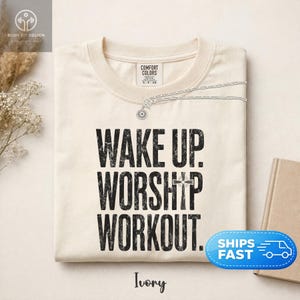 Könnte beinhalten: Ein elfenbeinfarbenes T-Shirt mit Rundhalsausschnitt und schwarzem, abgenutztem Schriftzug WAKE UP. WORSHIP WORKOUT., wobei ein Kreuzsymbol den Buchstaben I in WORSHIP ersetzt. Das T-Shirt hat ein Markenetikett von Comfort Colors am Halsausschnitt.