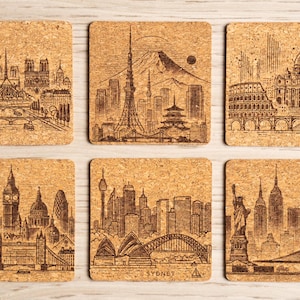 May include: Set of six square cork coasters with etched cityscapes. Each coaster features a different iconic skyline, including Paris, Tokyo, Rome, London, Sydney, and New York City. The coasters are a natural tan color.