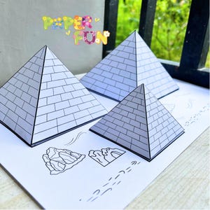 May include: Three paper pyramids with a brick pattern are displayed on a white surface. The pyramids vary in size, with the largest in the back and the smallest in the front. The words "PAPER FUN" are written in colourful letters above the pyramids.