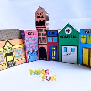May include: A colorful paper city set featuring buildings labeled "SCHOOL", "HOTEL", "CITY HALL", "FIRE DEPARTMENT", "HOSPITAL", and "POLICE". The buildings are various colors, including orange, pink, red, green, and blue. The words "PAPER FUN" are also visible.
