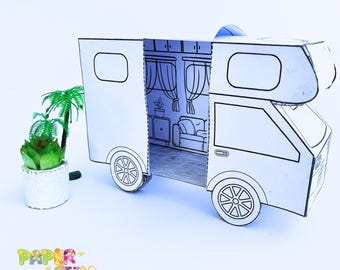 Puede incluir: Un modelo de papel blanco de una autocaravana con la puerta abierta, que revela un interior sencillo con muebles. El modelo está sobre una superficie blanca con una pequeña planta en maceta en primer plano.