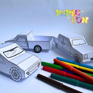 May include: Three paper car models, a pickup truck and two cars, ready to be coloured. The cars are on a white surface with a set of colourful markers.