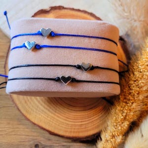 Könnte beinhalten: Drei Freundschaftsarmbänder mit silbernen Herzanhängern. Die Armbänder sind schwarz, blau und hellblau.