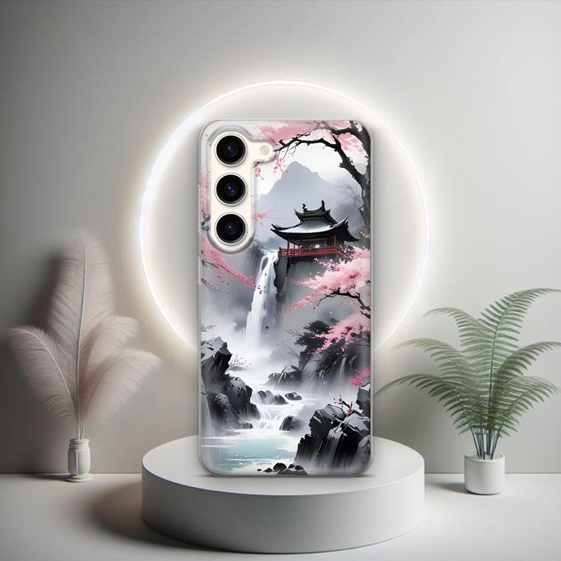 Puede incluir: Una funda para tel&eacute;fono con un dise&ntilde;o de acuarela de una pagoda japonesa, flores de cerezo y una cascada. La funda tiene un fondo negro y presenta un recorte para una c&aacute;mara de tres lentes.