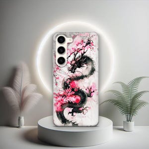 Puede incluir: Una funda transparente para tel&eacute;fono con un dise&ntilde;o de drag&oacute;n blanco y negro y flores de cerezo rosas. La funda tiene un recorte para la c&aacute;mara con tres lentes.