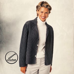 May include: A dark charcoal gray crochet cardigan featuring a collared neckline, long sleeves, and a front button closure with four white buttons. The garment is worn over a white ribbed turtleneck sweater and light gray trousers. Includes a crochet logo.