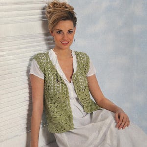 Op de afbeelding: Een lichtgroen gehaakt vest met een open ontwerp. Het vest wordt gedragen over een witte blouse en jurk. Het gehaakte vest heeft een knoopsluiting en een delicaat, kantachtig patroon. De algehele stijl is casual en vrouwelijk.